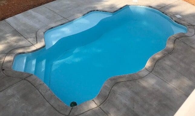 Kidney-shaped swimming pool with clear blue water on a concrete surface.