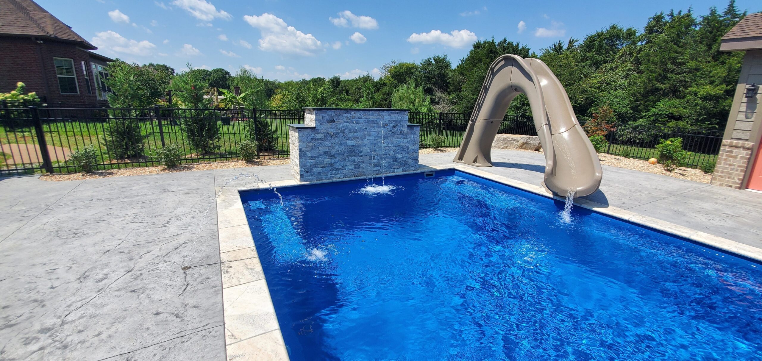 Backyard swimming pool with a slide and water feature on a sunny day.